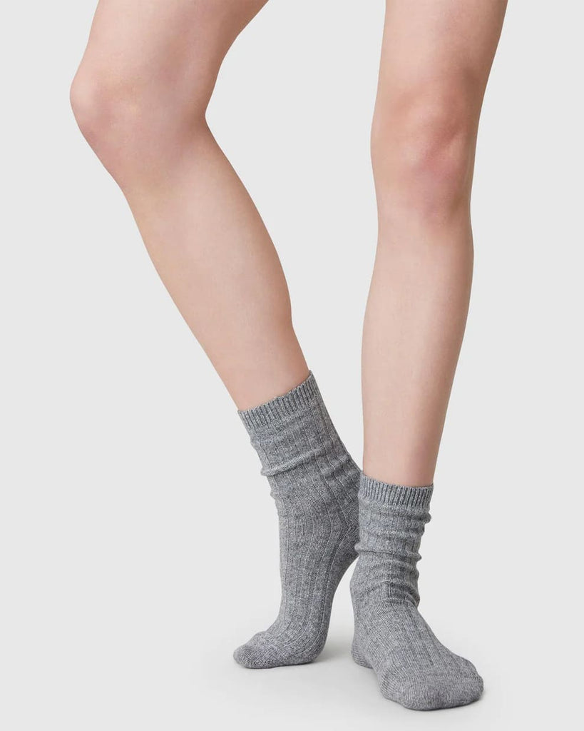 Une femme porte les chaussettes grises fabriquées en Italie, en coloris gris, de face, un pied relevé. 