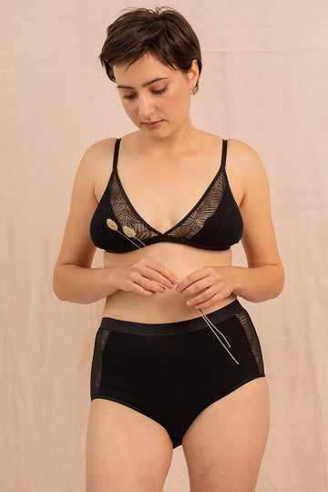 Jeune femme portant un ensemble de lingerie noir, le modèle de la culotte est taille haute. Avec un détail de tulle recyclé et le reste en coton biologique 