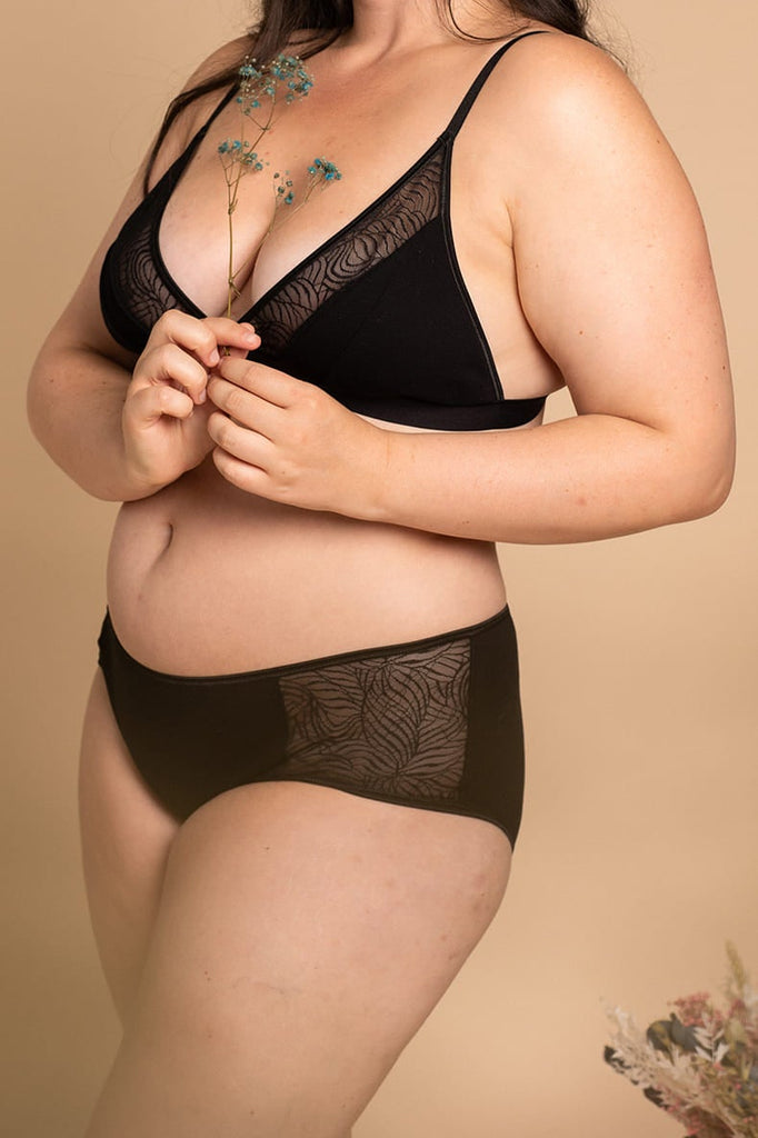 Jeune femme porte un ensemble de lingerie noir composé d'un soutien-gorge et d'un shorty en coton bio.